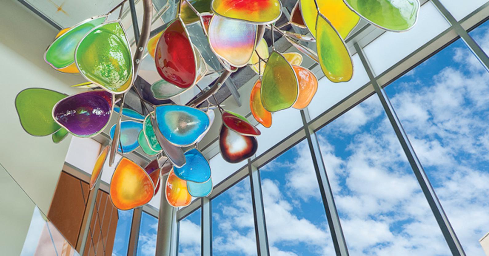 A sculpture suspended from the ceiling resembles a tree branch with leaves created from colored glass.